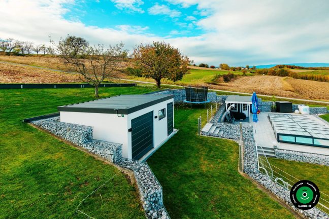 Garázs gabionokkal körülvéve és gondozott zöld gyepfelülettel