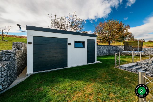 Garázs félnyeregtetővel rendezett zöld és lejtős környezetben