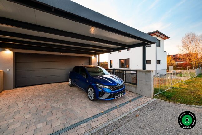 Garázs előtetővel a ház mellett parkoló kék autóval