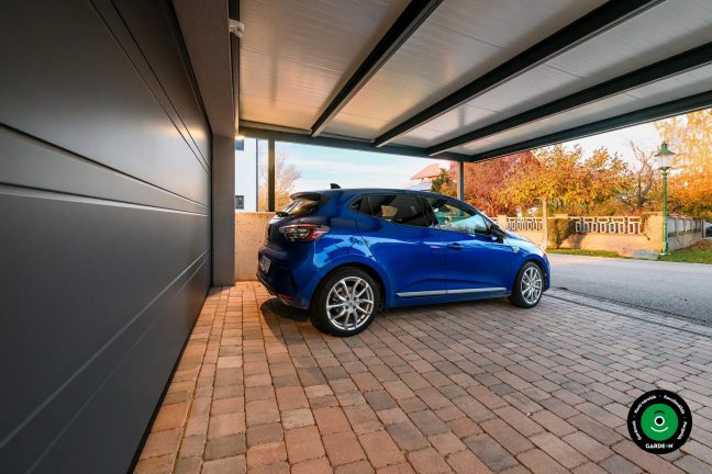 Kék autó az előtető alatt a nagy garázs mellett