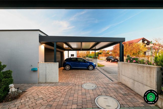 Autó az előtető alatt betonfalnál és kert mellett