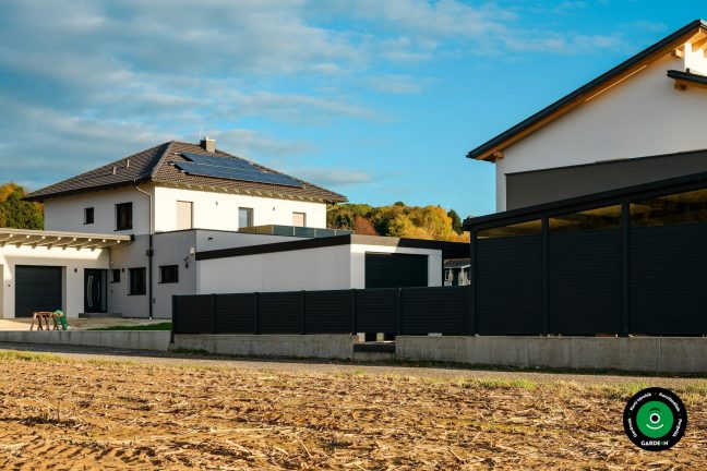 Modern garázs a családi háznál sötét kerítéssel