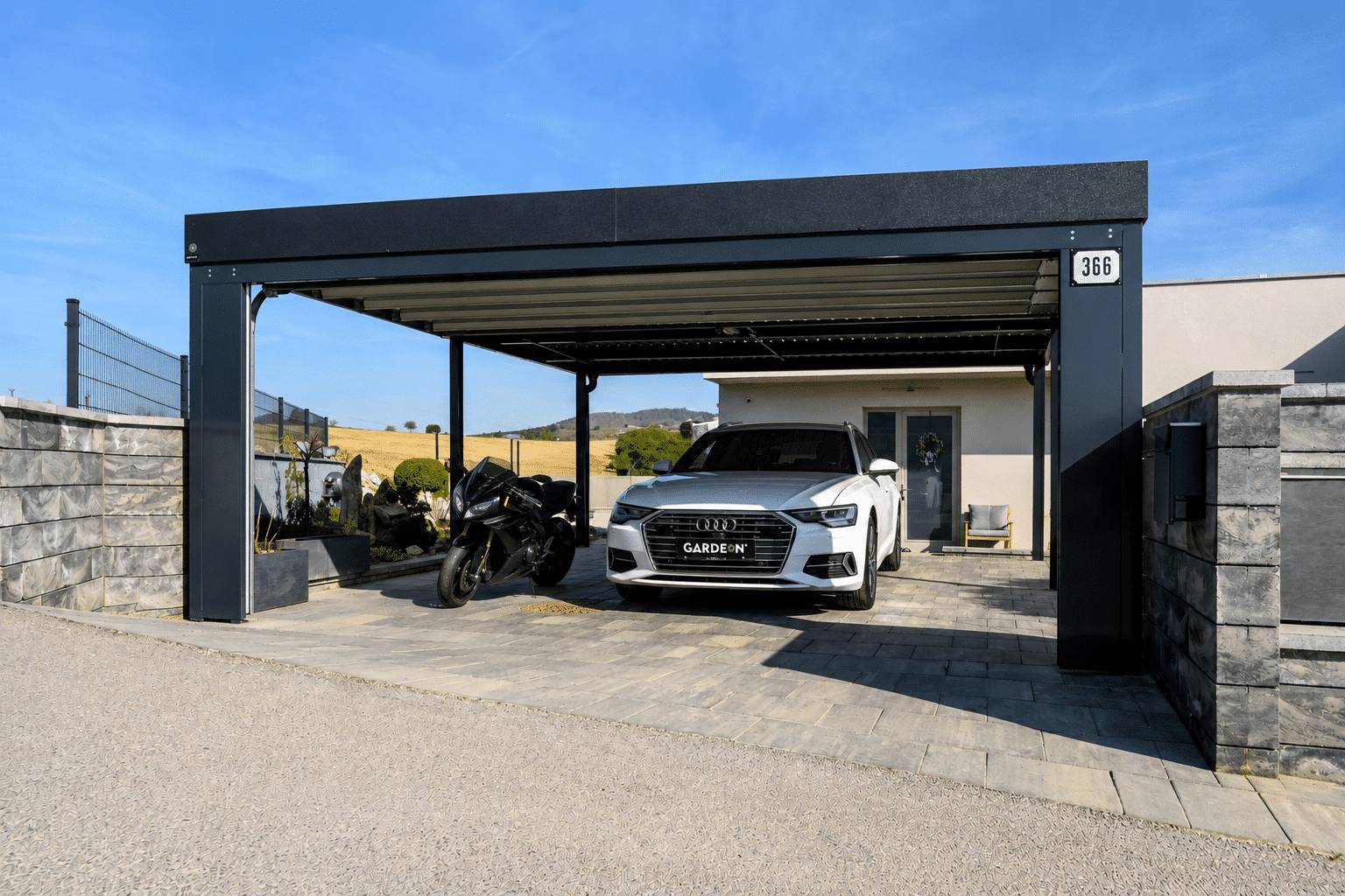 Gardeon kocsibe&aacute;ll&oacute; aut&oacute; &eacute;s motorker&eacute;kp&aacute;r egyidejű t&aacute;rol&aacute;s&aacute;ra, letisztult fekete ac&eacute;lszerkezettel, kő ker&iacute;t&eacute;s mellett