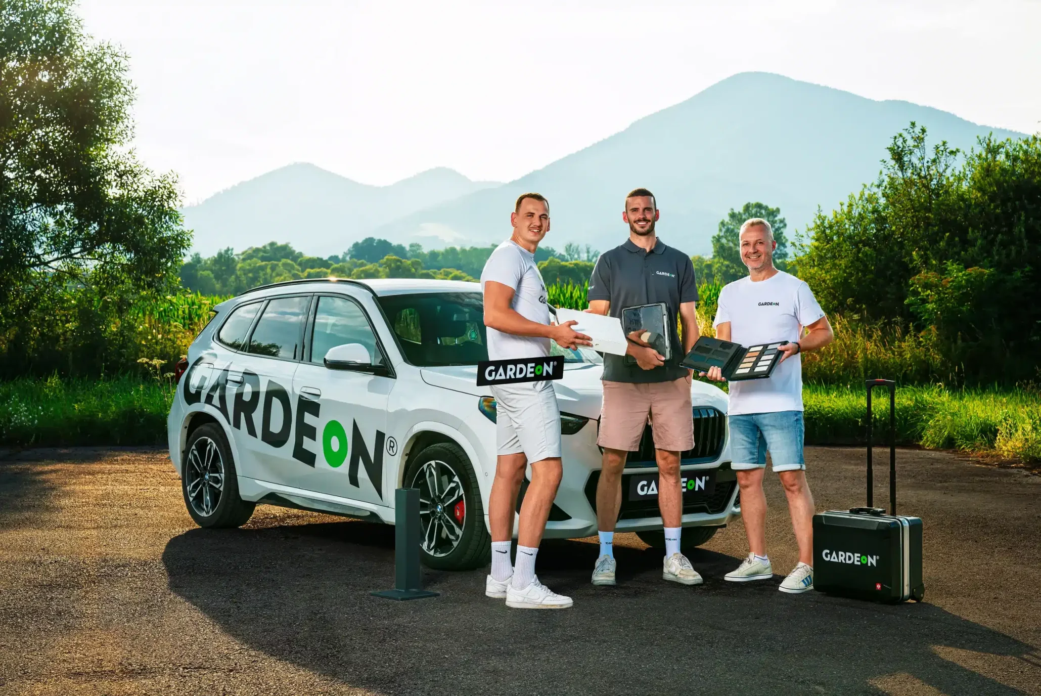 Három GARDEON ügynök anyagokkal és táskával a cég BMW-jénél.