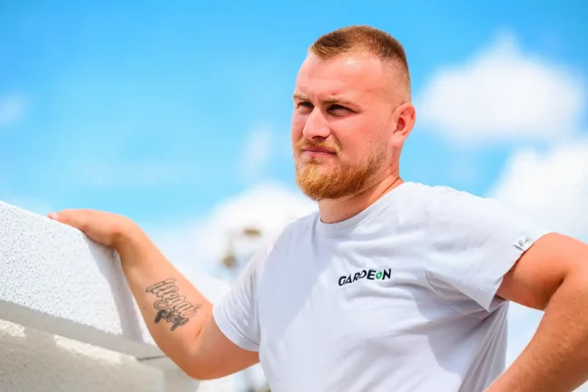 Portré egy GARDEON szerelőről, aki a garázs fehér falának támaszkodik