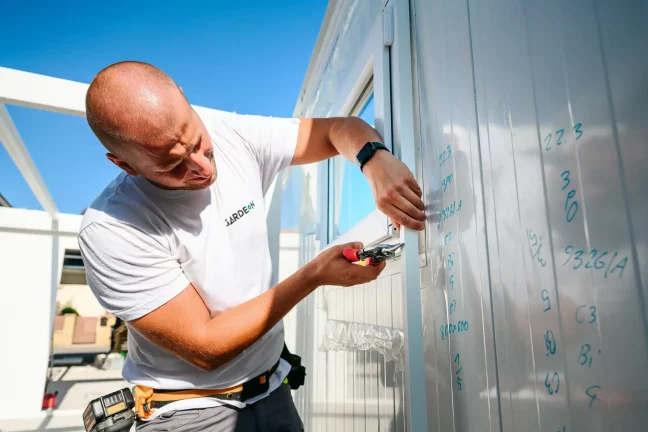 Egy munkatárs ollóval méretre vágja a fehér panel szélét az ablakkeretnél