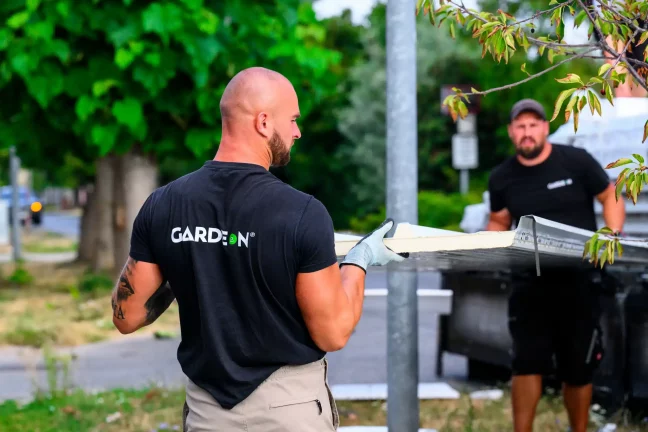 Két GARDEON munkatárs közösen visz egy falpanelt az utca mentén