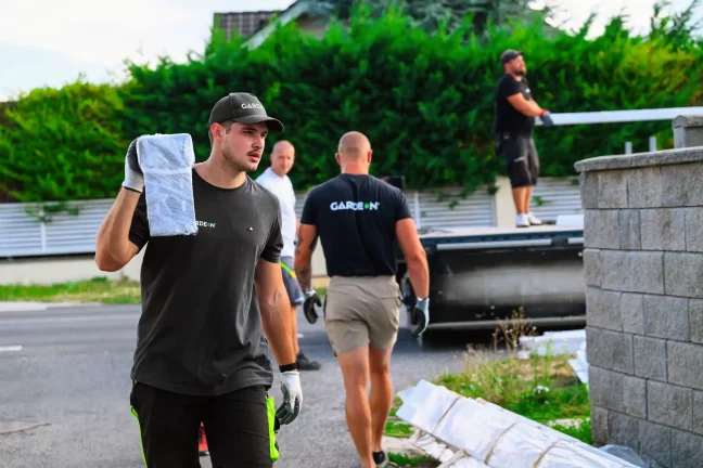 Egy szerelő csomagolt panelt visz a vállán a kőfal mellett