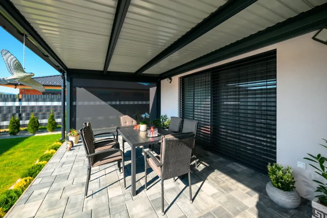Egy lamellás tetős pergola belső nézete, kerti székekkel és kilátással a zöld kertre