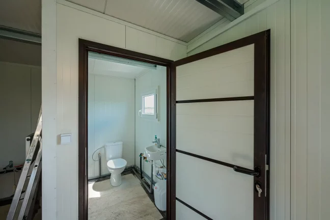 Kilátás a nyitott ajtón keresztül egy kis fürdőszobába WC-vel