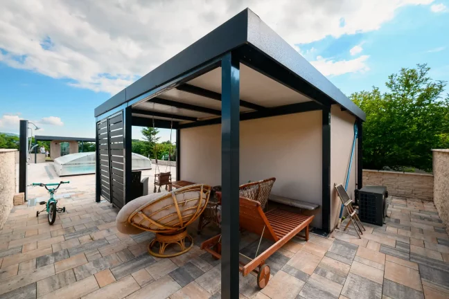 Antracit színű pergola egy ajtós kerti tároló mellett, kerékpárral és kerti bútorokkal alatta