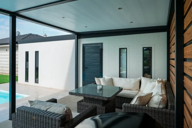 Kanapé és üvegasztal a pergola alatt, a sötét ajtók mellett