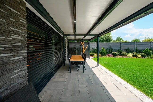 Étkezőasztal a pergola alatt, a ház kőburkolata mellett