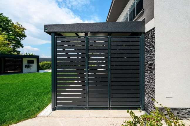 A pergola zárt fekete lamellás kapujának részlete a ház mellett