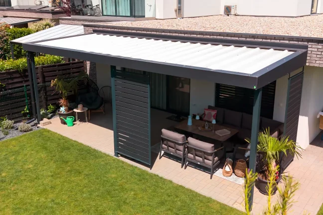 Pergola kerti bútorokkal egy sötét homlokzatnál, burkolt terasszal