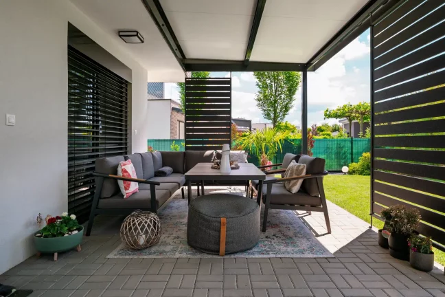 Kilátás egy antracit színű pergola belsejéből kerti bútorokra és oldalelemekre