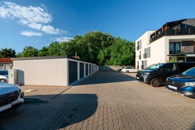 Sorgarázs parkolóval, autókkal és fehér társasházzal